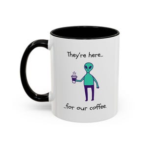 Puede incluir: Taza de café de cerámica blanca con asa e interior negros. La taza presenta un extraterrestre de dibujos animados sosteniendo una taza de café, con el texto "They're here... for our coffee."