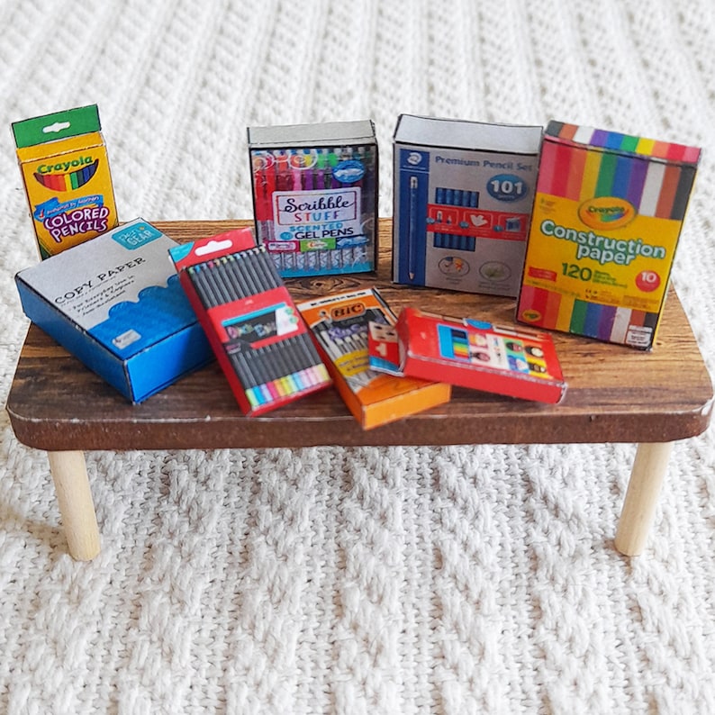 May include: A miniature wooden table with a variety of miniature art supplies, including Crayola colored pencils, construction paper, gel pens, and pencils. The supplies are in their original packaging.