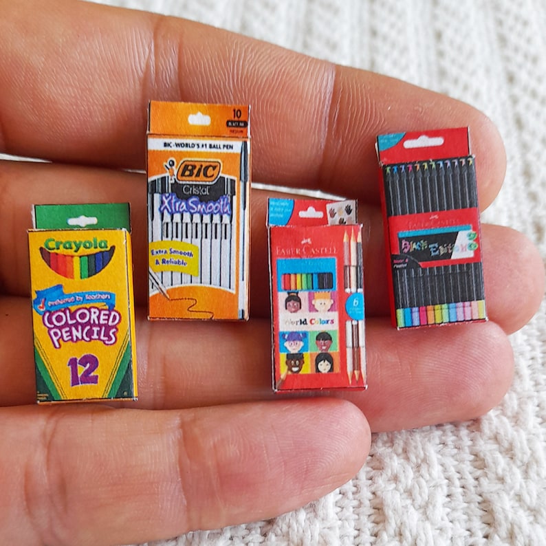 May include: A close-up of three miniature boxes of art supplies. The boxes are for Crayola colored pencils, Faber-Castell colored pencils, and BIC Cristal Xtra Smooth ballpoint pens. The boxes are all red, yellow, and blue.