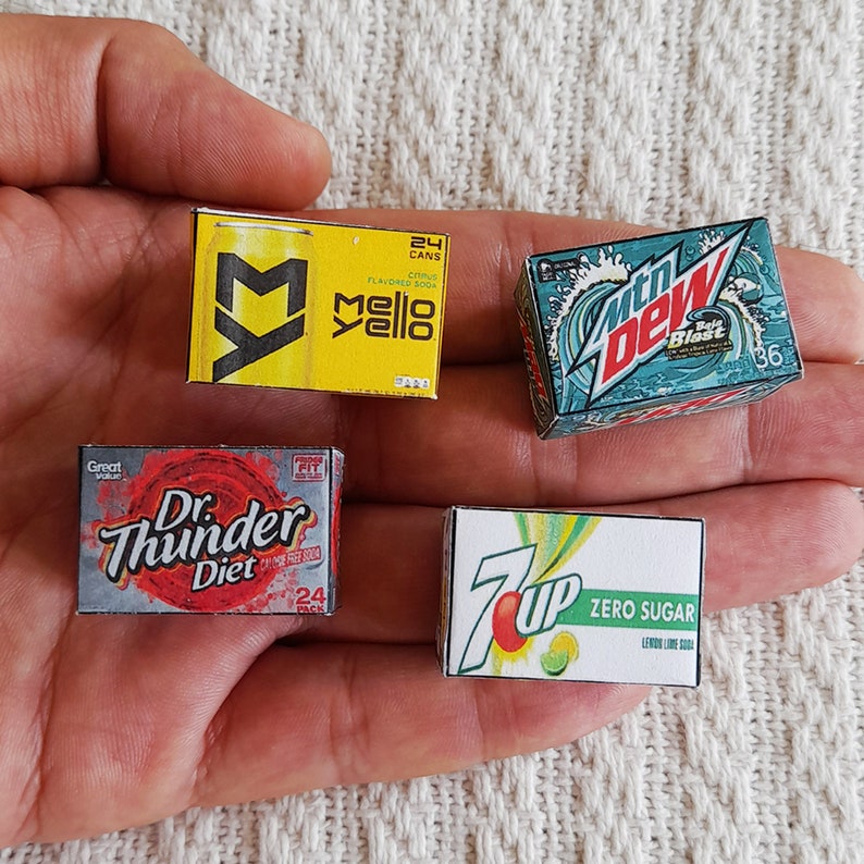 May include: Four miniature cardboard boxes of popular soda brands. The boxes are yellow, blue, grey, and white with the brand names Mello Yello, Mountain Dew, Dr. Thunder Diet, and 7 Up Zero Sugar.