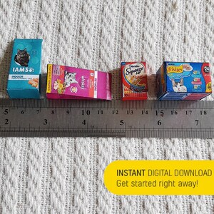 Pode incluir: Quatro caixas em miniatura de comida para gatos sobre uma superf&iacute;cie branca com uma r&eacute;gua. As caixas s&atilde;o das marcas IAMS, Whiskas, Delectables Squeeze Up e Friskies. A r&eacute;gua est&aacute; marcada em polegadas.