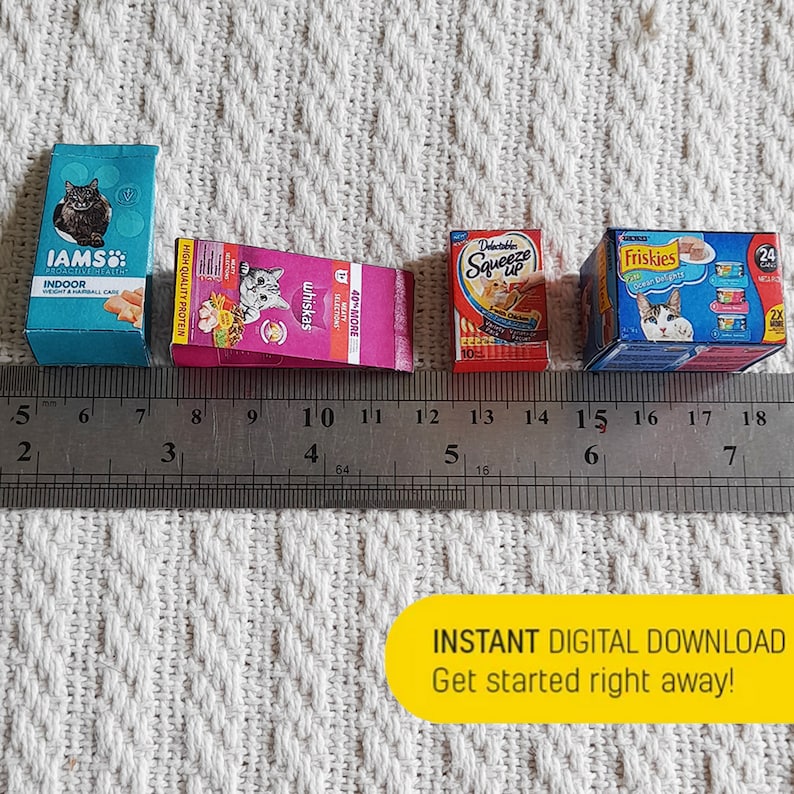 Pode incluir: Quatro caixas em miniatura de comida para gatos sobre uma superf&iacute;cie branca com uma r&eacute;gua. As caixas s&atilde;o das marcas IAMS, Whiskas, Delectables Squeeze Up e Friskies. A r&eacute;gua est&aacute; marcada em polegadas.