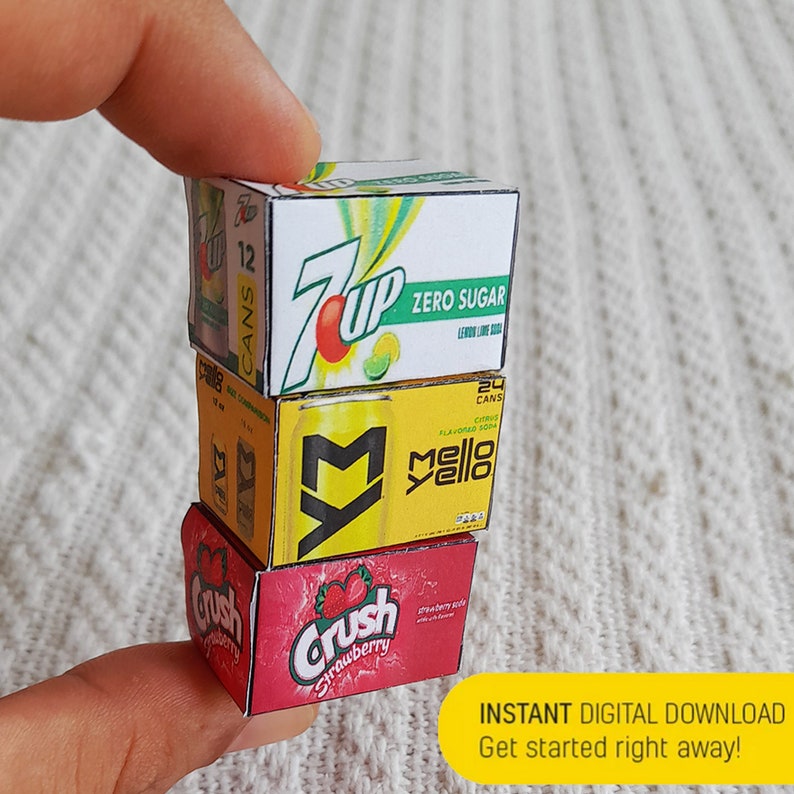 May include: A stack of four miniature cardboard boxes, each representing a different soda brand. The top box is green and white with the text "7 Up Zero Sugar Lemon Lime Soda". The second box is yellow with the text "Mello Yello Citrus Flavored Soda". The third box is yellow with the text "7 Up". The bottom box is red with the text "Crush Strawberry Soda".