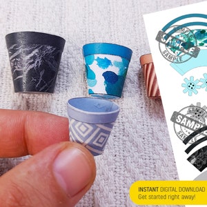 May include: Three miniature paper pots for planting. The pots are decorated with different patterns: black and white marble, blue and white watercolour, and a geometric pattern in shades of blue and white.
