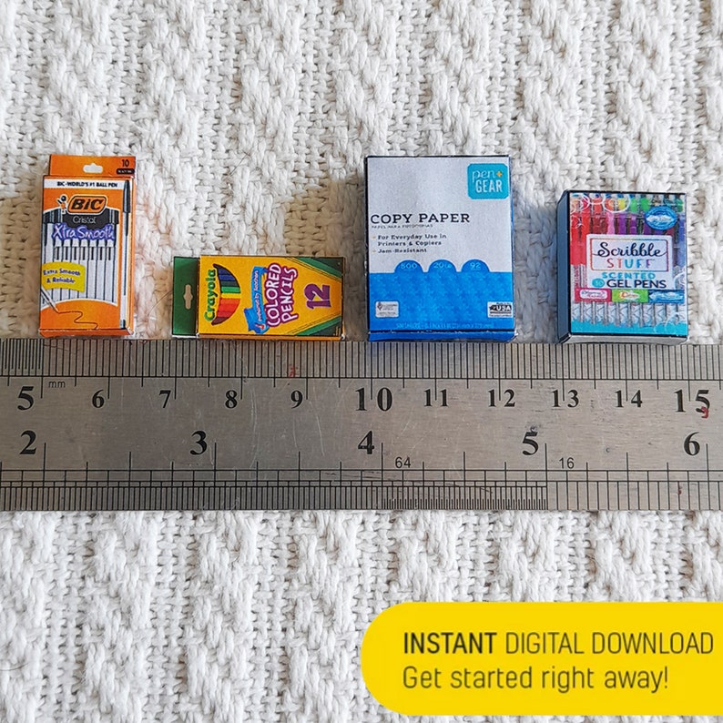 May include: Four miniature boxes of school supplies, including a pack of BIC Xtra Smooth pens, a box of Crayola colored pencils, a pack of copy paper, and a box of scented gel pens. The boxes are arranged in a row on a white surface with a ruler underneath.
