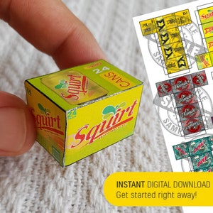 May include: A yellow and green cardboard box with the words "Squirt Thirst Quencher" and "24 Cans" printed on it. The box is a miniature replica of a soda can box.