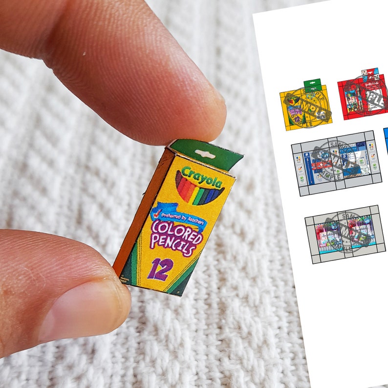 May include: A miniature box of Crayola colored pencils. The box is yellow with a red and blue stripe and the text "Crayola Colored Pencils 12" printed on it. The box is open and shows a row of 12 colored pencils.