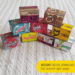May include: A collection of miniature cardboard boxes featuring various popular soda brands, including Coca-Cola, Crush, Mello Yello, 7 Up, Dr. Thunder, Squirt, and A&W Root Beer. The boxes are stacked and arranged on a white textured surface.