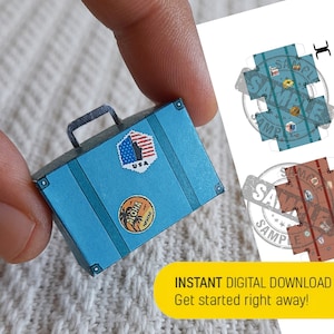 Puede incluir: Una maleta de papel azul con un asa negra. La maleta tiene pegatinas que dicen "USA" y "Aloha Hawaii".