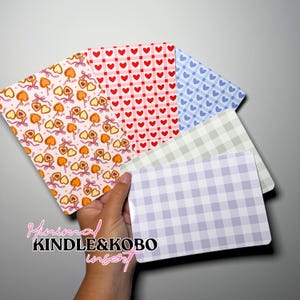 Könnte beinhalten: Ein Set aus fünf rechteckigen Einlegern für E-Reader mit verschiedenen Mustern, darunter orangefarbene Herzanhänger auf hellrosa Grund, rote Herzen auf weißem Gitter, blaue Herzen auf weißem Gitter, hellgrünes Vichy-Karo und hellviolettes Vichy-Karo.