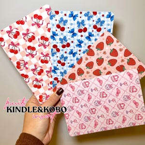 Peut inclure: Quatre inserts rectangulaires pour liseuse présentant des motifs distincts : un damier rose et blanc avec des cerises rouges, un vichy bleu et blanc avec des cerises et des nœuds, un fond pêche avec des fraises et un motif rose avec des boules à facettes.