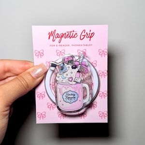 Könnte beinhalten: Ein magnetischer Griff für E-Reader, Handys und Tablets auf einer rosa Präsentationskarte mit Schleifenmuster. Der Griff zeigt eine rosa Tasse mit der Aufschrift Hockey Romance Fuel, verziert mit Schlagsahne, einem Eishockeyhelm und einem Schläger.