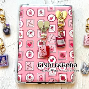 Pode incluir: Corrente de pingentes rosa Kindle e Kobo com um padrão rosa e branco de corações, velas e flechas. A corrente de pingentes tem fechos em forma de coração dourados e prateados e vários pingentes, incluindo um livro, uma vela e uma carta de baralho. O texto "KINDLE&KOBO charm chain" é visível.