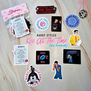 Può includere: Una collezione di adesivi con le frasi "Kiss All The Time" e "Disco, Occasionally". Gli adesivi includono immagini di una palla da discoteca, una lista e una persona. La tavolozza dei colori comprende rosa, nero e blu.
