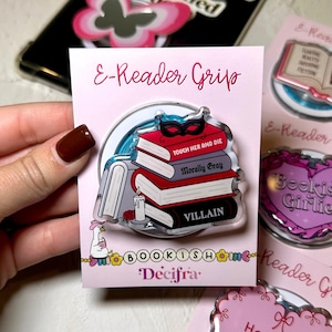 May include: An acrylic e-reader grip on a light pink backing card labeled E-Reader Grip. The grip features a stack of three books with a black masquerade mask on top. The book spines are labeled Touch Her and Die, Morally Gray, and Villain.