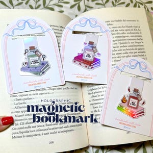 Pode incluir: Três marcadores de página magnéticos em cartões brancos arqueados com ilustrações de fitas azuis. Cada um apresenta um adesivo holográfico de uma garrafa de vidro sobre livros, rotulada como Mystery & Murder, Love & Lust e Heat & Spice.