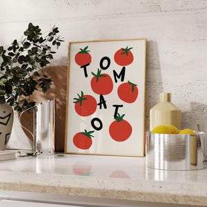 May include: A white framed print with the word "TOMATO" spelled out in red letters with red tomato illustrations surrounding the letters.