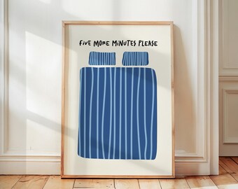 May include: A framed art print with a blue striped bed illustration and two pillows. The text "FIVE MORE MINUTES PLEASE" is written above the bed illustration in black. The artwork is displayed on a wooden floor.