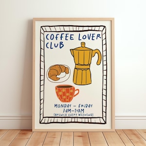 Può includere: Una stampa incorniciata a tema caffè. L'opera presenta una caffettiera gialla, un croissant e una tazza di caffè rossa con motivi floreali. Le parole "COFFEE LOVER CLUB" sono in alto, con orari e giorni di apertura in basso.