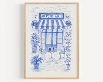 Puede incluir: Impresión en acuarela azul y blanca de un café parisino, "Au Petit Paris", con un toldo a rayas, una mesa pequeña, sillas y plantas en macetas. La obra de arte está enmarcada.