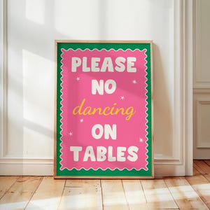 May include: A framed poster with a pink background and the text "PLEASE NO dancing ON TABLES" in white and yellow. The poster has a green border and is displayed on a wooden floor.