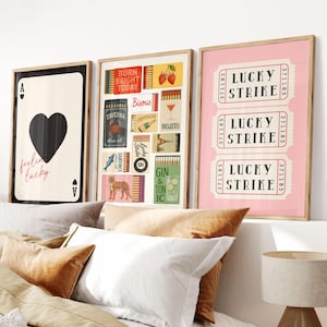 May include: Three framed art prints. The first features a black heart on a cream background with the text "feelin lucky". The second has various vintage-style illustrations. The third displays three pink "Lucky Strike" tickets.