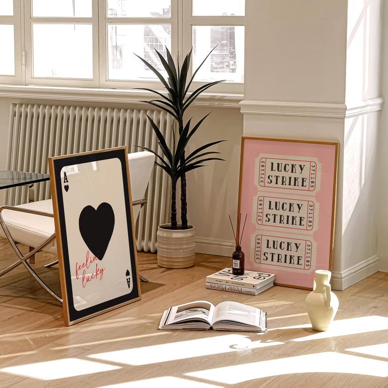 May include: A framed playing card with a black heart and the words "feeling lucky" in pink. A pink framed print with "Lucky Strike" text is displayed. A tall potted plant and a vase are also in the room.