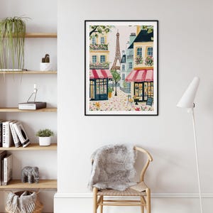 May include: Watercolor painting of a Parisian street scene with the Eiffel Tower in the background. Buildings with pink awnings and flower boxes line the cobblestone street. A black framed art print adds a touch of Parisian charm to any space.
