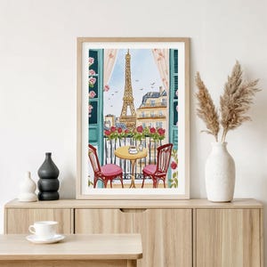 May include: Watercolor print of a Parisian balcony scene. The Eiffel Tower is visible through an open window with red roses, a small table, and two chairs. The artwork is framed in a light wood frame.