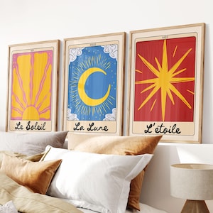 Op de afbeelding: Drie ingelijste tarotkaarten. De eerste heeft een gele zon met roze stralen, de tweede een blauwe achtergrond met een gele maan, en de derde een rode achtergrond met een gele ster. Elke print heeft Franse tekst.