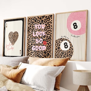 May include: Three framed wall art prints featuring a playing card with a leopard print heart and the text feeling lucky, a leopard print background with the text YOU LOOK SO GOOD and a red lip icon, and two eight balls with leopard print.