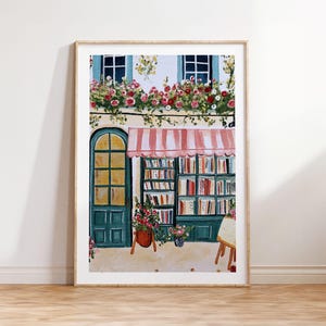 Könnte beinhalten: Ein gerahmtes Aquarellgemälde eines malerischen Buchladens. Das Gebäude hat eine türkisblaue Tür und Fensterrahmen, eine gestreifte Markise und eine Ausstellung von Büchern. Rote und rosa Blumen schmücken die Fenster und Töpfe und verleihen der Szene Farbe.