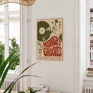 May include: A rectangular wall poster featuring a dark green vinyl record and a hand operating a turntable tonearm. The text reads MIDNIGHT GROOVES, SPINNING AFTER DARK, and JAZZ, DISCO, SOUL, FUNK in red and black on a light beige background.