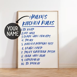 Könnte beinhalten: Ein gerahmter Druck mit dem Text "HAILEY'S KITCHEN RULES" in blauer Schrift. Die Regeln beinhalten "Sei nett", "Iss gut" und "Koche mit Liebe". Eine runde Grafik zeigt, wo ein Name hinzugefügt werden kann.