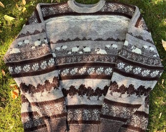 May include: A long-sleeve crew neck sweater featuring a knit pattern of sheep, trees, and foliage in shades of brown, gray, and cream. The garment has a ribbed collar, cuffs, and hem, with horizontal bands displaying repeating nature motifs.