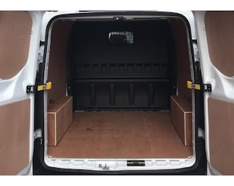 May include: Interior view of a white cargo van with open doors. The cargo area features brown plywood paneling on the floor and side walls. Two rectangular wooden boxes are visible, and the back wall is black.