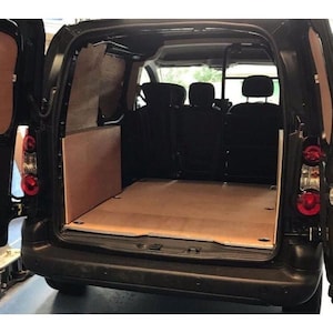 May include: A black van with the rear doors open, showing a wooden floor and side panels. The interior has black seating and a partition, indicating a cargo or work vehicle. The taillights are visible on both sides of the vehicle.
