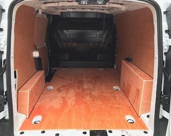 May include: Interior view of a white cargo van with a wooden floor and side paneling. The van's cargo area features a light brown plywood floor and side walls, with two rectangular wooden boxes. The back wall is black.