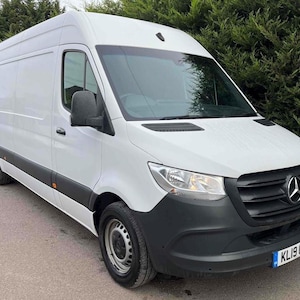 May include: A white Mercedes-Benz Sprinter van with a black front bumper and grill. The van has a high roof and a side door. The license plate reads KL19 OTG. The van is parked on a paved surface.