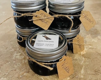 May include: Six small glass jars filled with dark brown vanilla bean paste, tied with twine and labeled with handwritten tags. The labels read "Marns Tark", "Kraken", "Kraken", "Vodka", and "vanilla bean paste Homemade - Small Batch 1 tsp paste = 1 tsp extract".