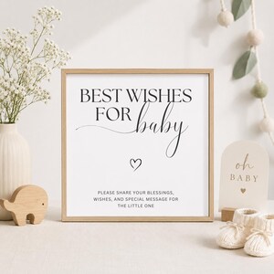 以下が含まれることがあります： 「BEST WISHES FOR baby」の黒い筆記体とハートのシンボルが描かれた額入りのサイン。小さなサインには「oh BABY」と書かれています。ベビーブーツと木製のゾウも写っており、ベビーシャワーや保育園のテーマを示唆しています。