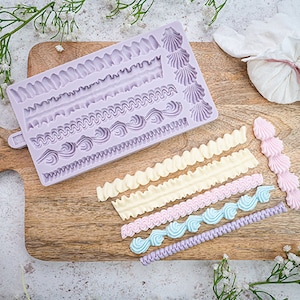 May include: A purple silicone mold with various border designs for decorating cakes and pastries. The mold is on a wooden cutting board with examples of piped frosting borders in different colors.