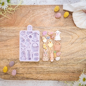 Könnte beinhalten: Eine violette Silikonform mit verschiedenen Ostermotiven, darunter Hasen, Küken, Eier und Körbe. Neben der Form liegen mehrere dekorierte Zuckerkekse in den gleichen Formen.