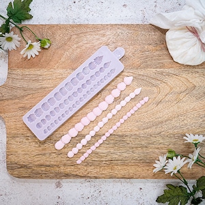May include: A purple silicone mould with a row of different sized shell shapes.  Four rows of pink fondant shells are arranged on a wooden chopping board.