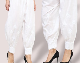 Può includere: Pantaloni bianchi in cotone con ricami floreali e un bordo in pizzo bianco nella parte inferiore delle gambe. I pantaloni sono raccolti alle caviglie.