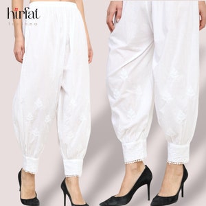 May include: White cotton pants with embroidered floral designs and a white lace trim at the bottom of the legs. The pants are gathered at the ankles.