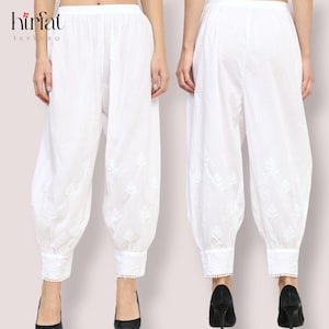 May include: White cotton pants with embroidered floral details and lace trim at the bottom. The pants are loose fitting and have a wide leg.
