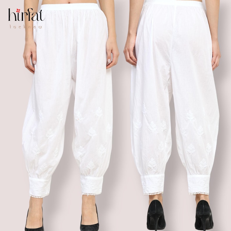 May include: White cotton pants with embroidered floral details and lace trim at the bottom. The pants are loose fitting and have a wide leg.