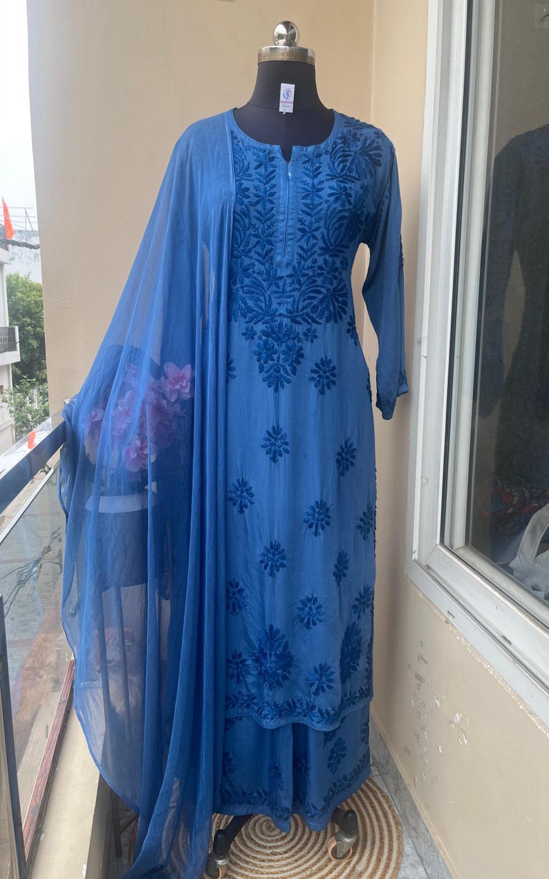 May include: A blue embroidered salwar kameez set displayed on a mannequin. The set includes a long tunic with floral embroidery, matching pants, and a sheer dupatta. The outfit is a solid blue color.
