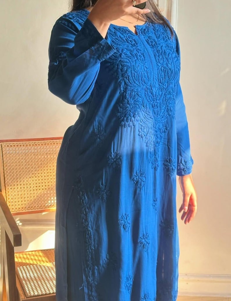 May include: A long, flowing, blue dress with intricate floral embroidery. The dress features long sleeves and a notched neckline. The embroidery is concentrated around the neckline and down the front, with additional floral patterns scattered across the fabric.